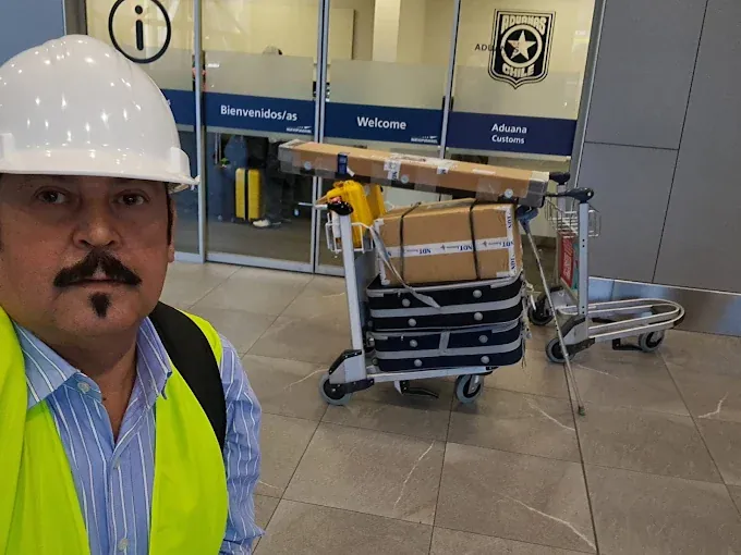 Agente de aduanas en el aeropuerto con un carro con cajas frente a la oficina de Aduanas de Chile